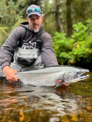 Man holding a large fish in a river, with lush greenery in the background.