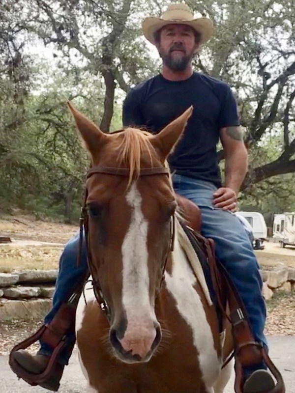 Man in cowboy hat riding a horse in a wooded area.