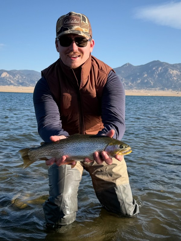 Person holding a fish in knee-deep water with mountains in the background.